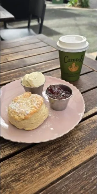 A scone with jam and lavender cream beside a green Campos cup
